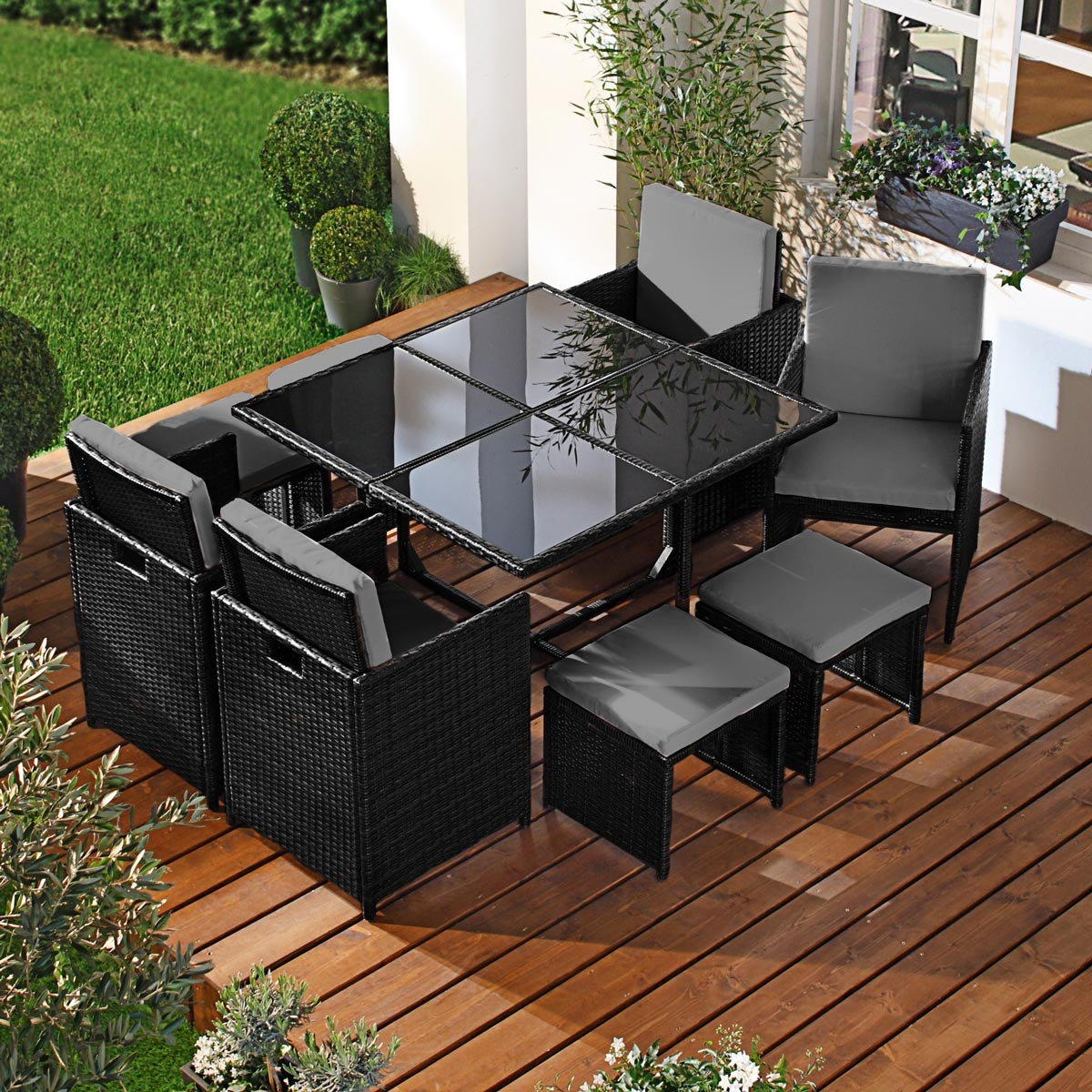 Schwarze Polyrattan Gartengarnitur mit Glas-Tischplatte, 4 Stühlen und 4 Hockern auf Holzterrasse.