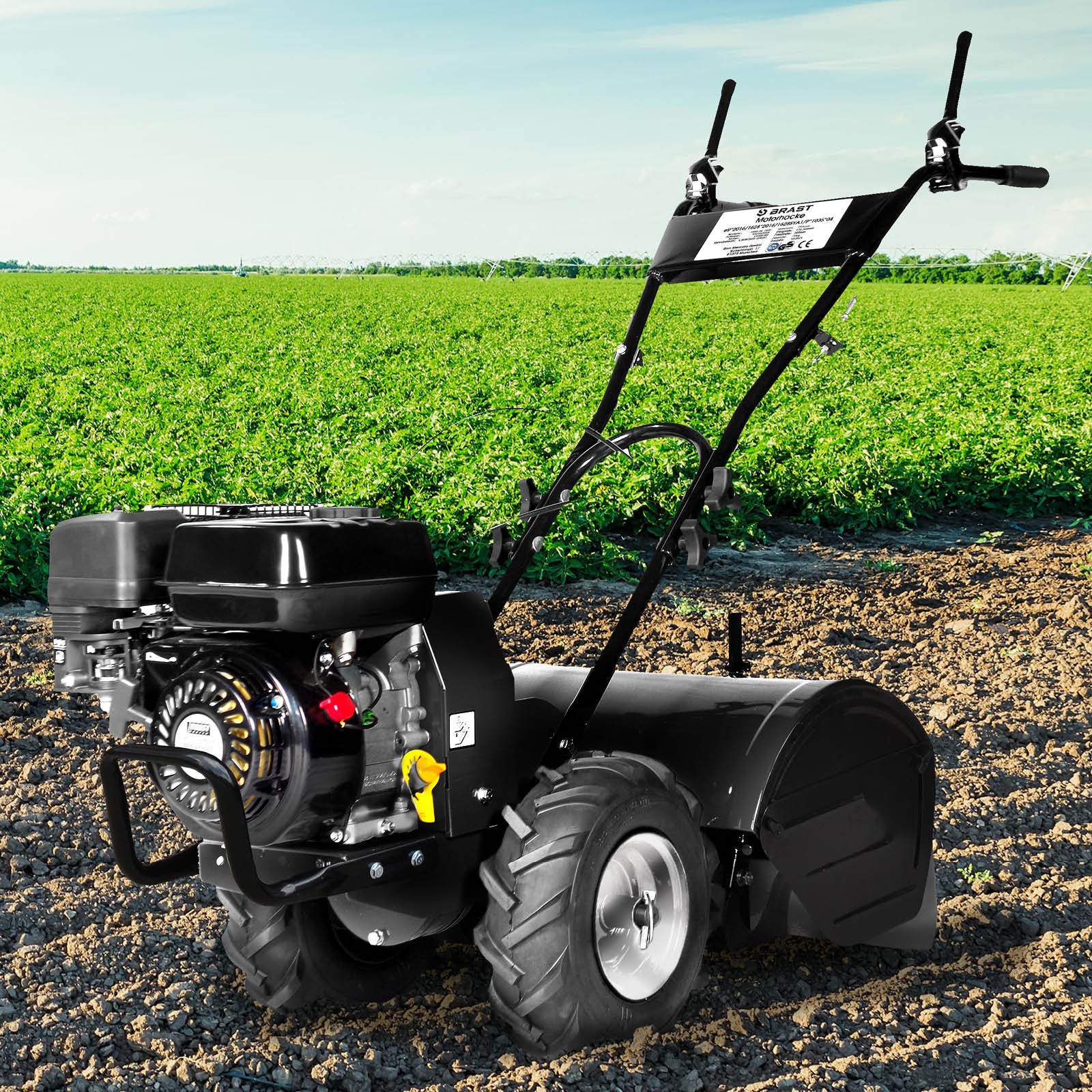 Schwarze Benzin Gartenfräse mit Motorhacke, großen Reifen und Bodenfräse Pflug vor grünem Feld.