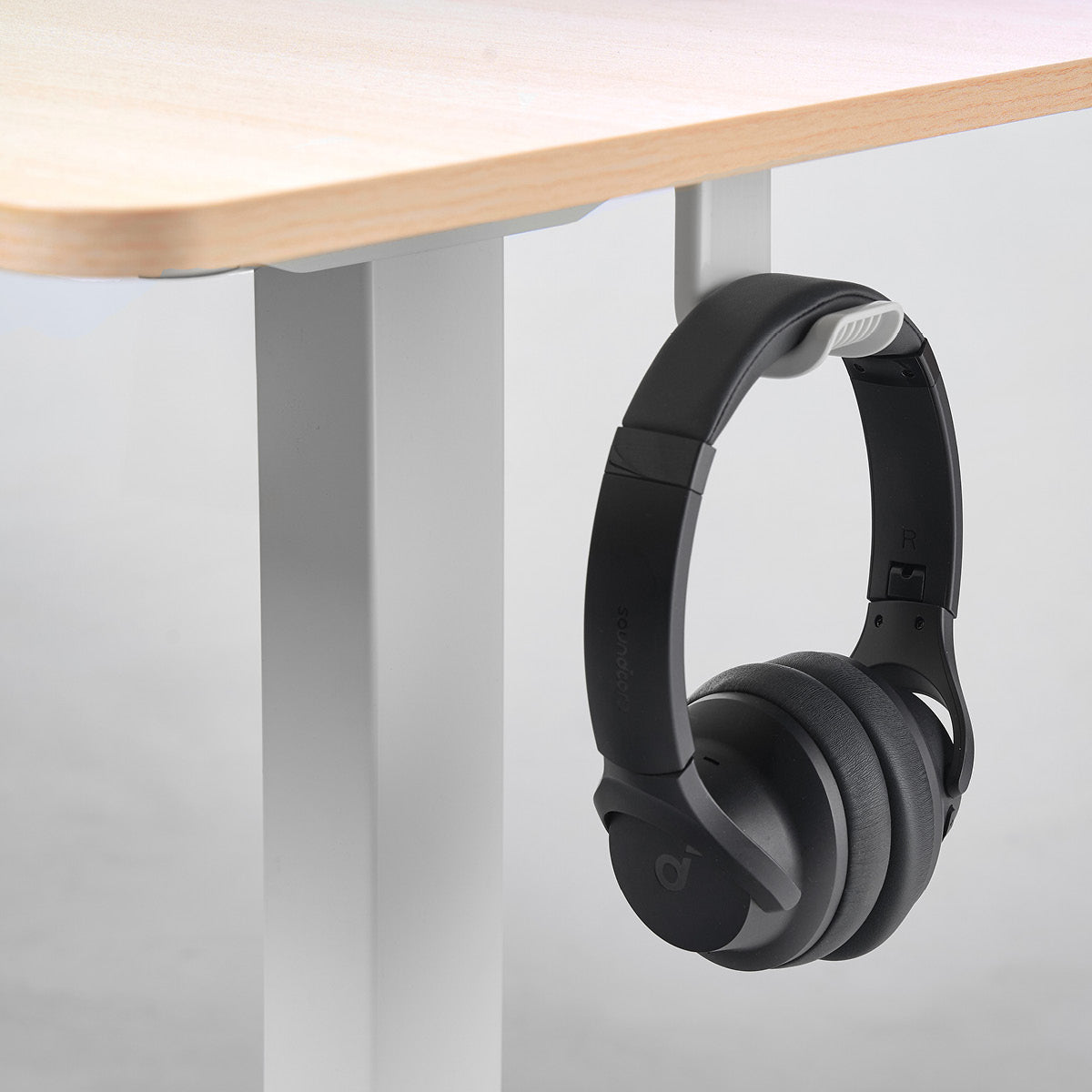 Höhenverstellbarer Schreibtisch FlexxPro mit ahornfarbenem Holz und weißem Metallgestell, schwarzer Kopfhörerhalter am Tisch .