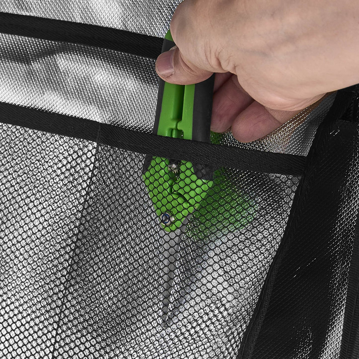 Hand greift grünes Gartenscherenmesser durch schwarzen Netzstoff des GrowCube XL Komplettsets.